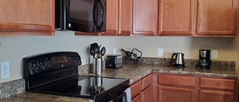 A kitchen with wooden cabinets, a black microwave, a stove, and granite countertops.