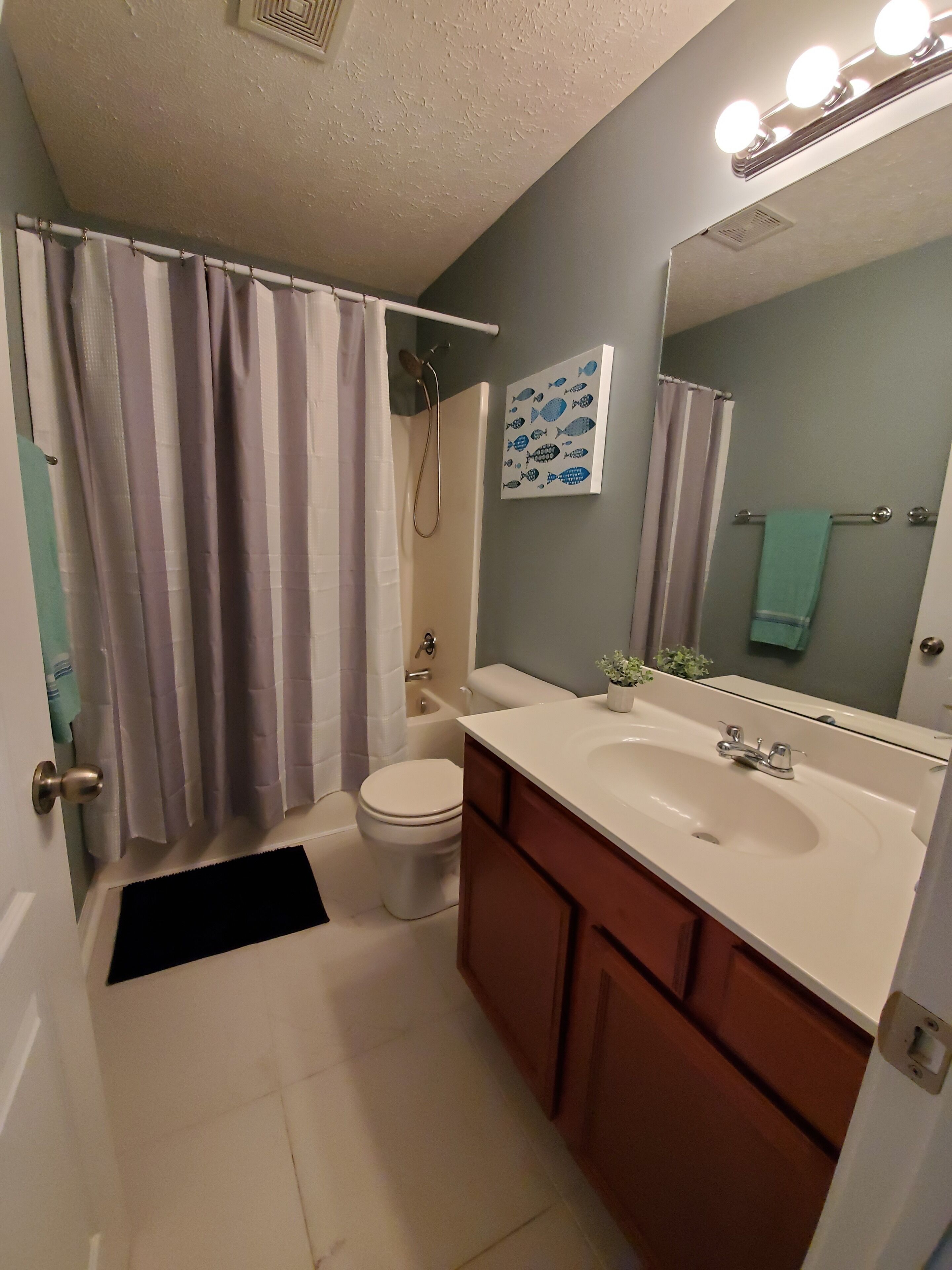 A bathroom with a shower, toilet, sink, and a mirror with lights.