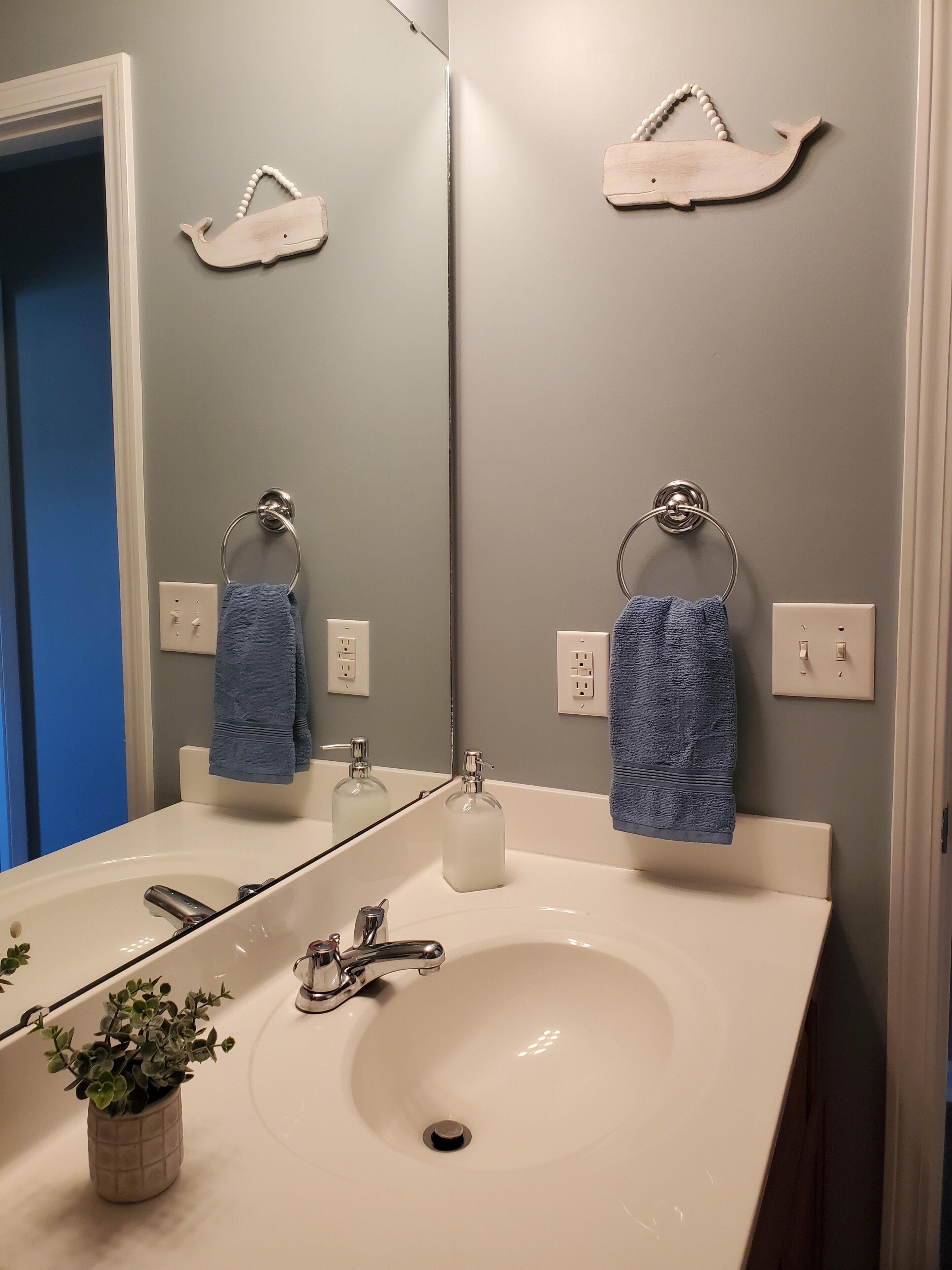 Un baño con un lavabo blanco, dos toalleros con toallas azules, un espejo y dos adornos de madera con forma de ballena en la pared.
