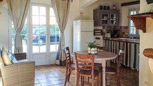 A cozy dining area with a round table and wooden chairs, a wicker sofa, and a view of parked cars through a glass door. - 2 bedroom gorgeous home in Roussillon (Roussillon)