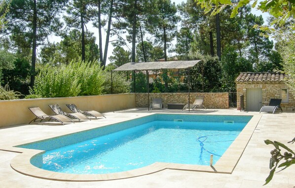 Piscina rectangular con borde de azulejos, rodeada de sillas de descanso y un muro de piedra.