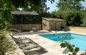 Una piscina con sillas de descanso, un edificio de piedra y una pérgola.