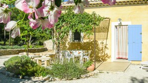 A garden with a pergola, a table, and chairs, a blue door, and a yellow building. - 2 bedroom gorgeous home in Roussillon (Roussillon)