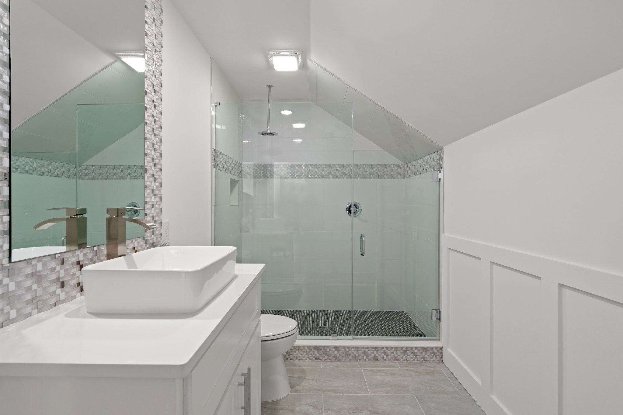 A modern bathroom with a large white sink, a glass-enclosed shower, and a tiled floor.