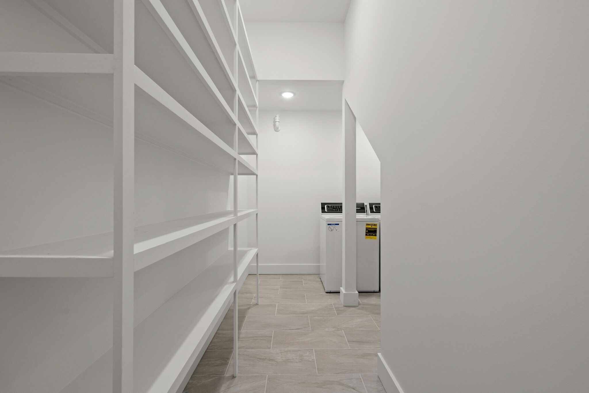 En stilren, modern hall med vita hyllsystem och en tvättstuga med staplade tvättmaskiner.