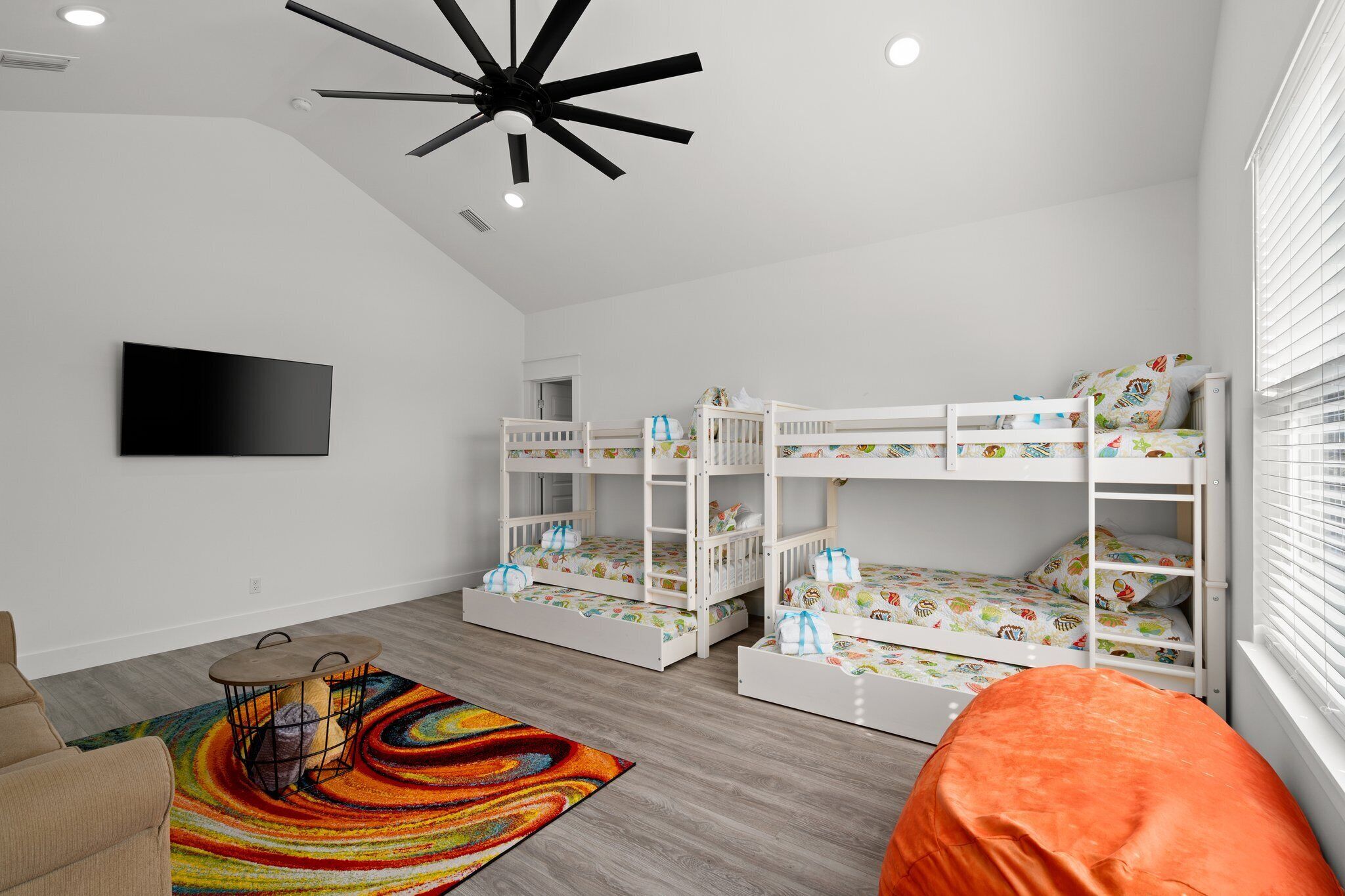 Camera per bambini con letti a castello, TV a schermo piatto, tappeto colorato e ventilatore a soffitto.