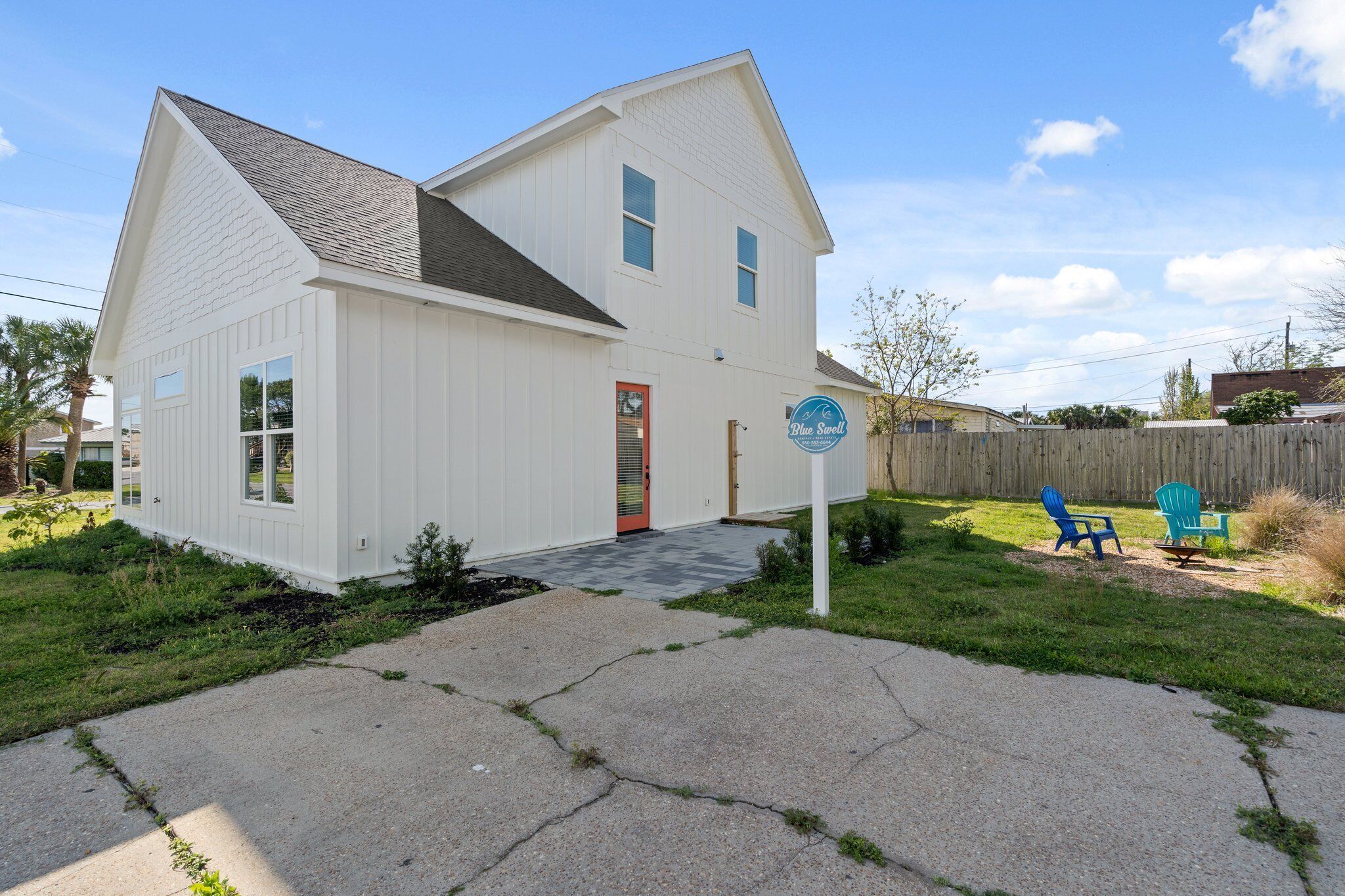 A white two-story house with a red door, a small front porch, and a sign that reads "Blue Swell."