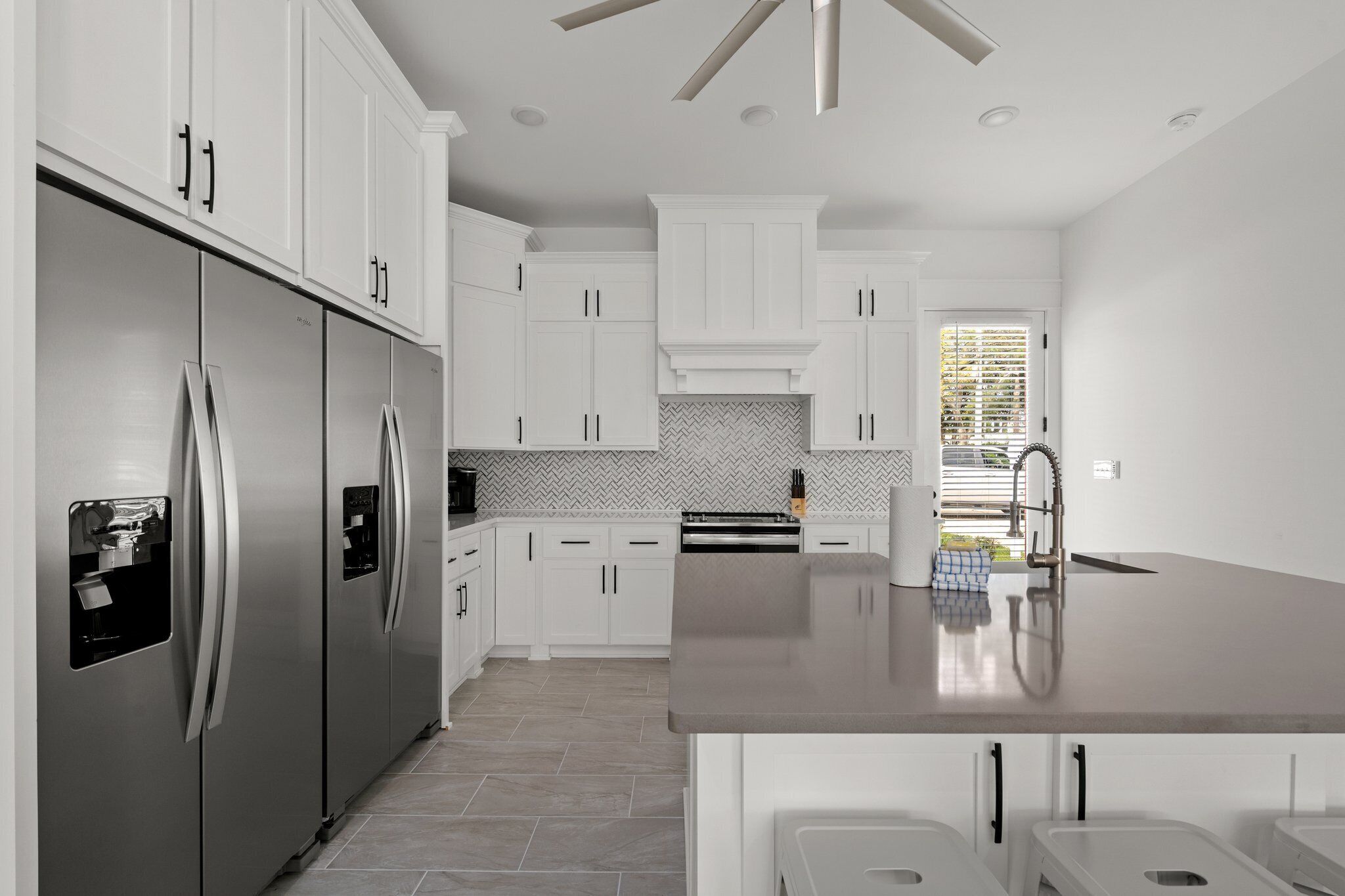 A modern kitchen with white cabinetry, stainless steel appliances, and a herringbone tile backsplash.