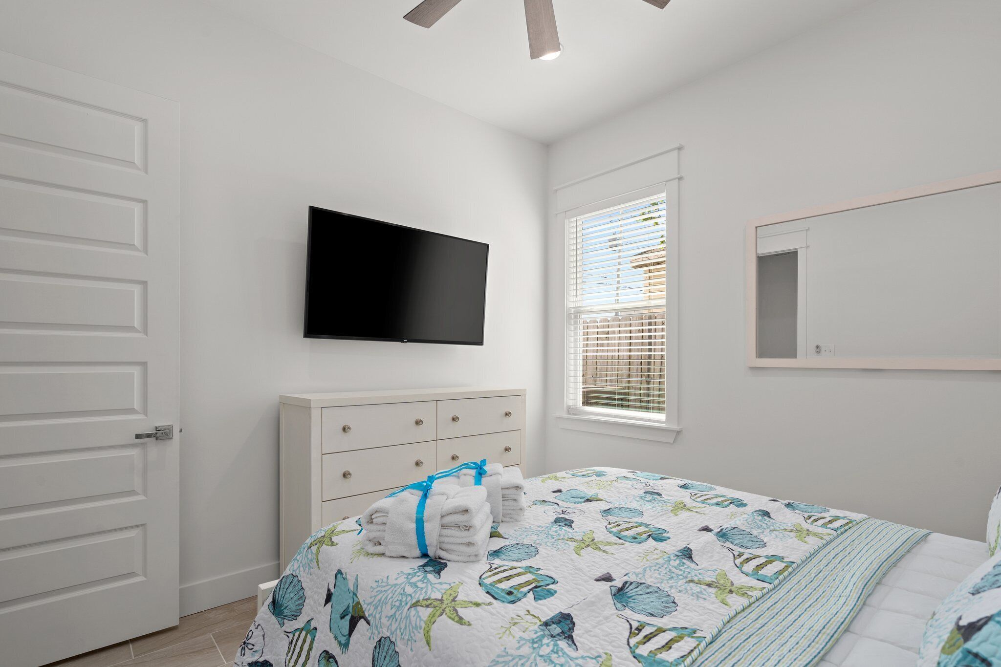 Une chambre à coucher comprenant un lit, un téléviseur à écran plat, une commode et une fenêtre avec des stores.