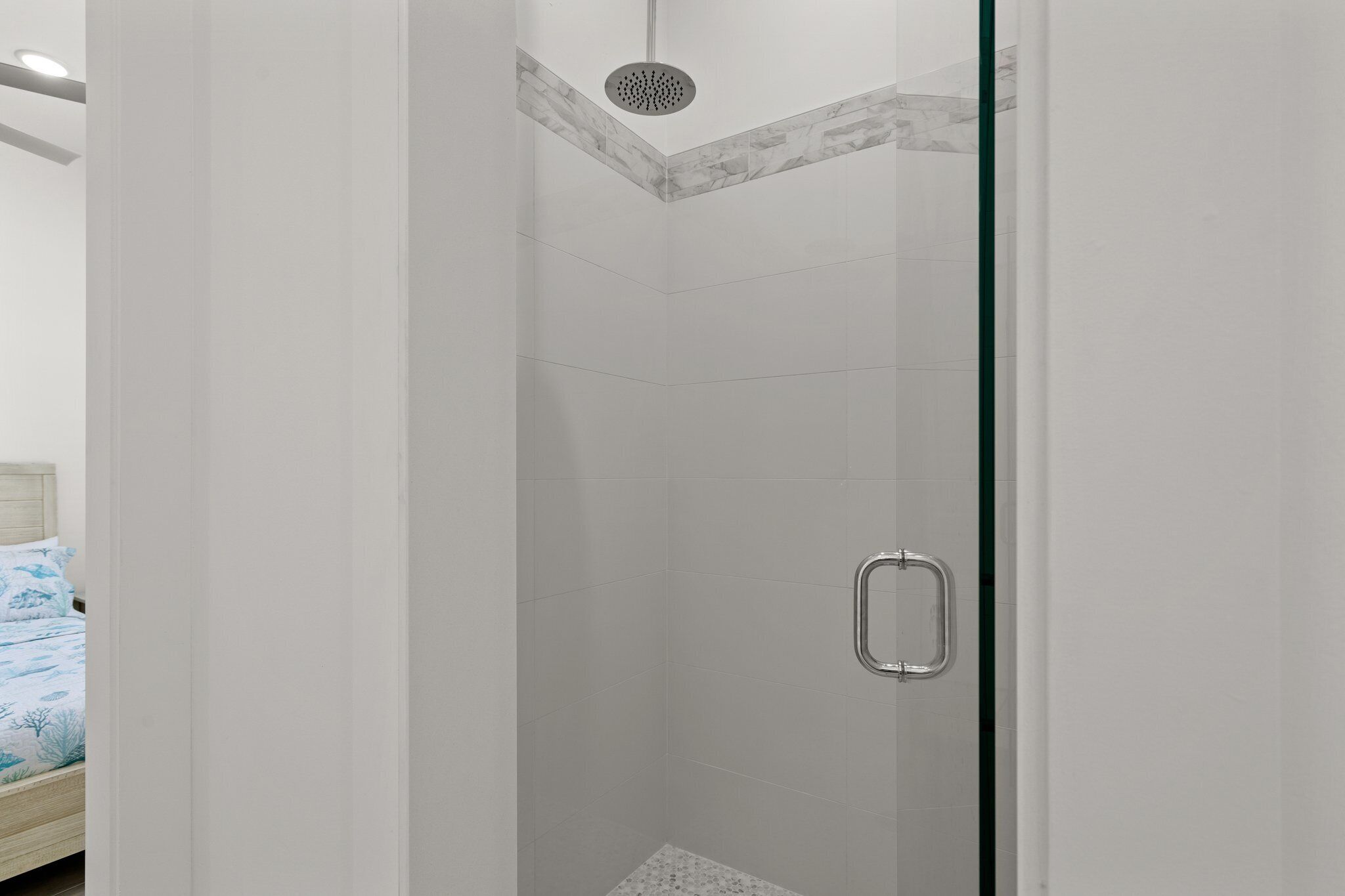 A glass-enclosed shower with a rain showerhead, a metal handle, and a tiled floor.