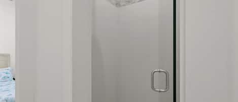 A glass-enclosed shower with a rain showerhead, a metal handle, and a tiled floor.