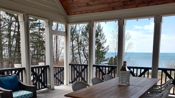 A wooden deck with a table and chairs, overlooking a body of water and trees.