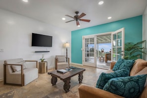 A living room with a sofa, armchair, coffee table, TV, and a ceiling fan.