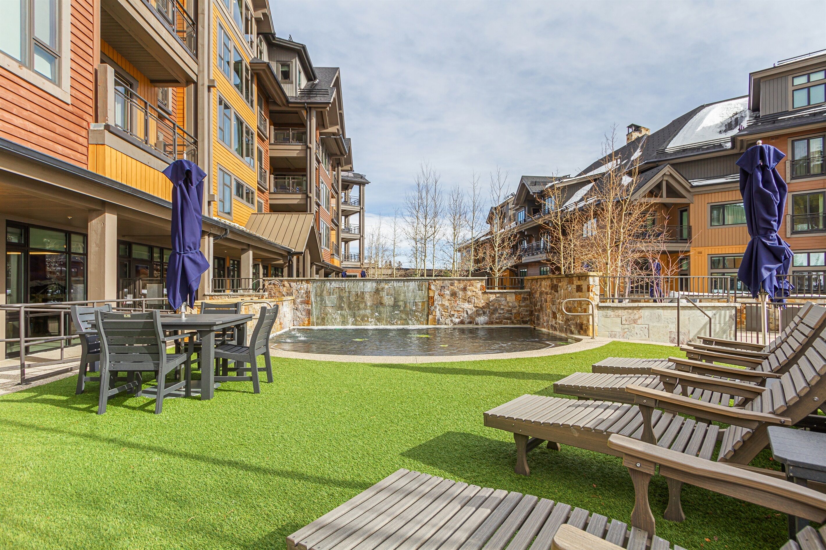 A courtyard with a pool, lounge chairs, and a table with chairs.