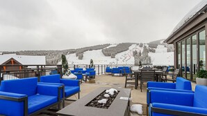 A snow-covered outdoor seating area with blue chairs and a stone fire table, overlooking a ski slope. - Grand Colorado on Peak 8 Suite - Ski-in/out (Breckenridge)