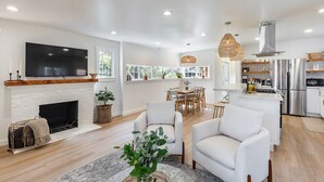 A modern living room with a fireplace, white sofas, and a dining area with a table and chairs. - Your wine country getaway! (Sonoma)
