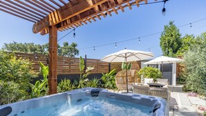 A hot tub with a wooden pergola overhead, surrounded by lush greenery and outdoor furniture. - Your wine country getaway! (Sonoma)