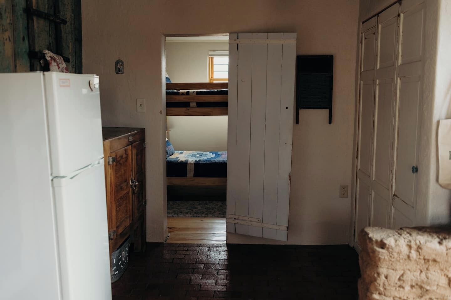 Ein schmaler Gang, der zu einem Schlafraum mit Etagenbetten, einem Kühlschrank und einem Holzschrank führt.