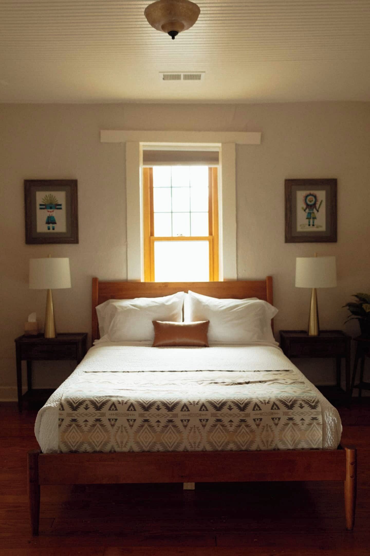 A neatly made bed with a patterned bedspread, two bedside lamps, and framed artwork on the walls.