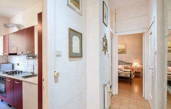 A narrow hallway with a kitchen on one side and a bedroom on the other. The kitchen has a stove, oven, and cabinets. The bedroom has a bed, nightstand, and lamp. - Gorgeous apartment in Genova with WiFi (Genova)