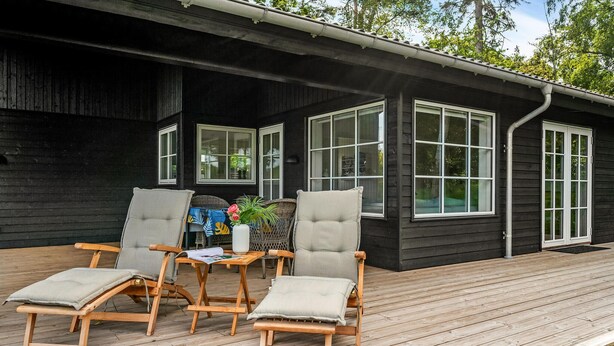 A wooden deck with two lounge chairs and a table, a black building with large windows, and a small garden area. - 3 bedroom lovely home in Gilleleje (Gilleleje)