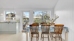 A dining area with a table set for four, surrounded by wooden chairs, in a room with white walls and large windows offering a view of the outside. - 3 bedroom lovely home in Gilleleje (Gilleleje)