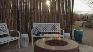 Un patio con una chimenea, dos bancos de metal blanco y una valla de bambú tejido.