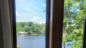 Une fenêtre donnant sur un lac, des chaises et un parasol rouge.