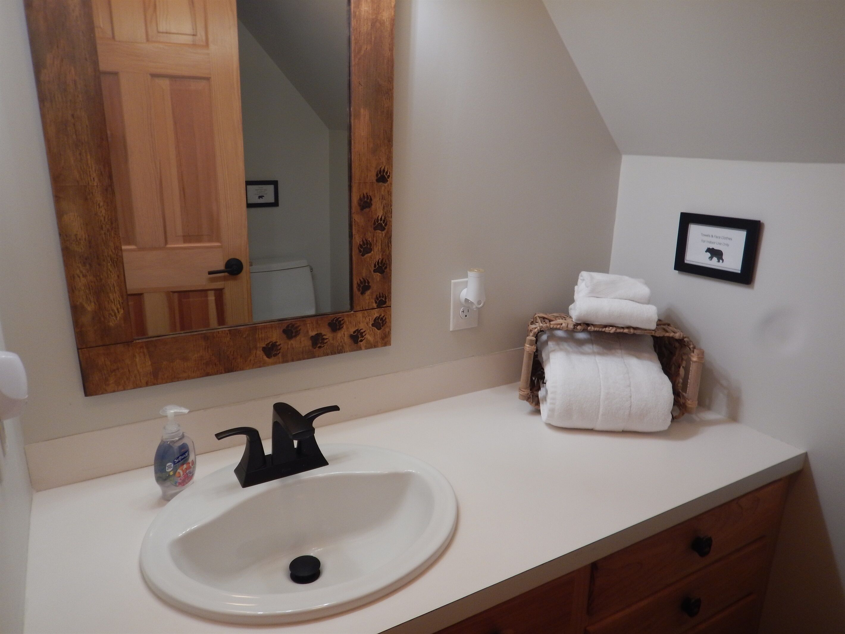 A bathroom with a white sink, a mirror with a wooden frame, a towel rack, and a framed picture on the wall.