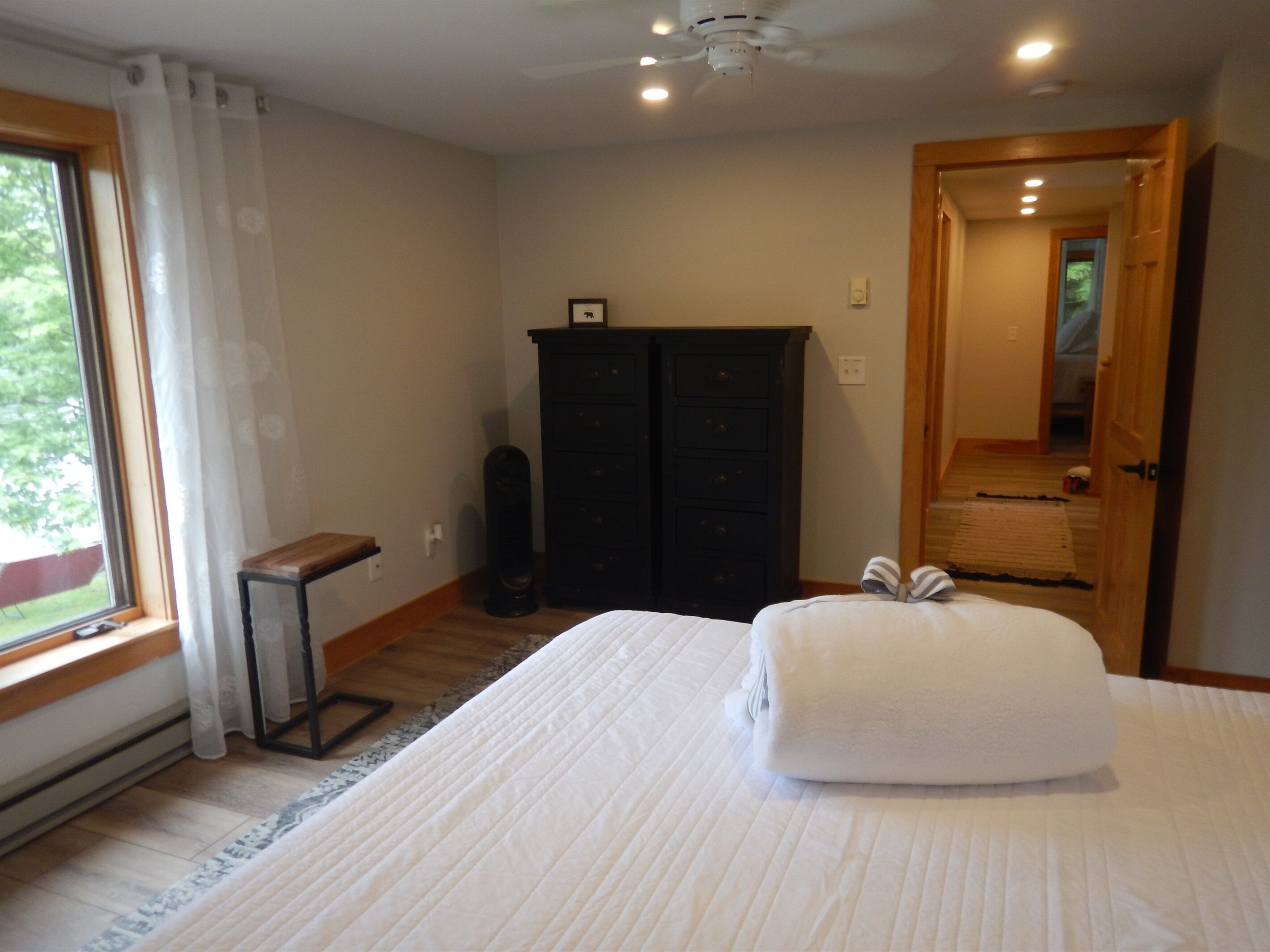A bedroom with a bed, a dresser, a ceiling fan, and a window with curtains.