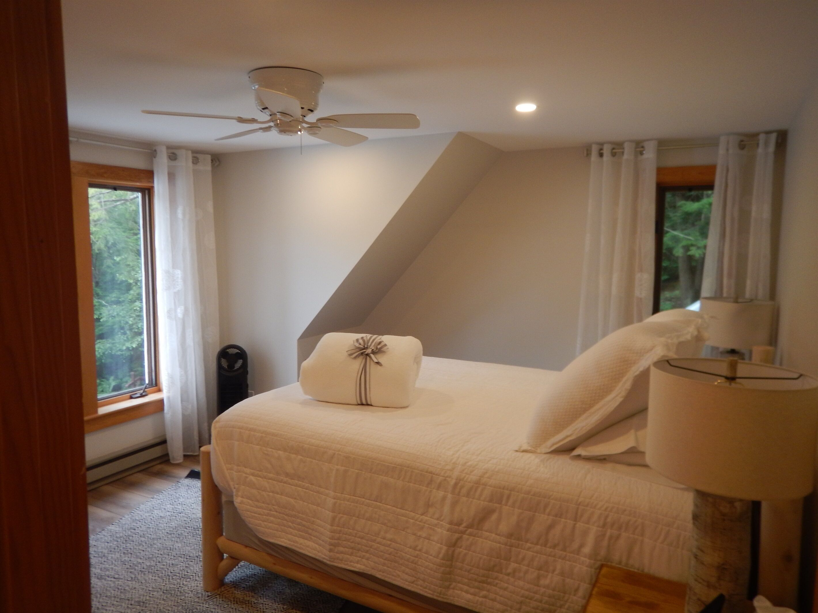 A bedroom with a bed, a ceiling fan, a window, and a lamp.