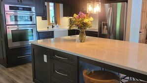 Une cuisine moderne avec des meubles de couleur sombre, des appareils en acier inoxydable, un grand îlot central doté de tabourets et un luminaire suspendu.