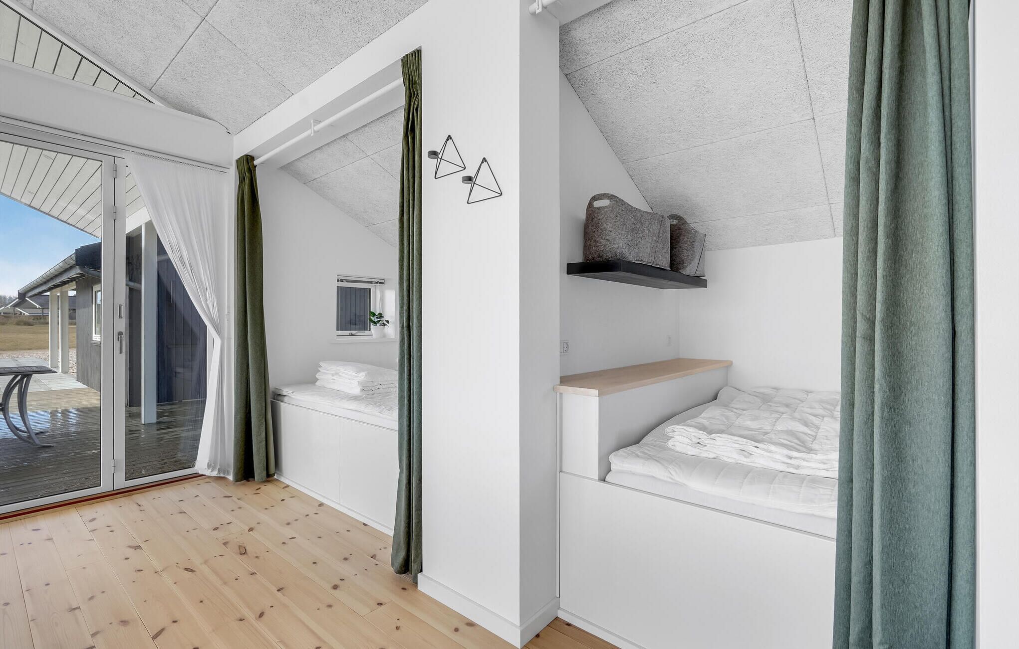 A modern, minimalist bedroom with a wooden floor, a bed with white bedding, a small bedside table, a shelf with a decorative item, and a window with a view of the outdoors.