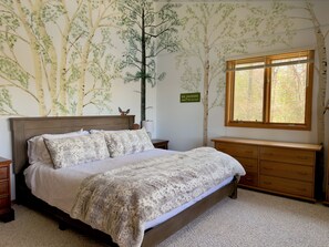 Une chambre à coucher avec un lit, des tables de chevet en bois, une commode, une fenêtre avec des stores et une fresque murale représentant des arbres.