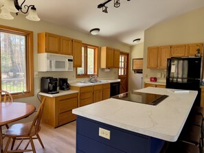 A modern kitchen with wooden cabinets, a white microwave, a black refrigerator, and a marble island.