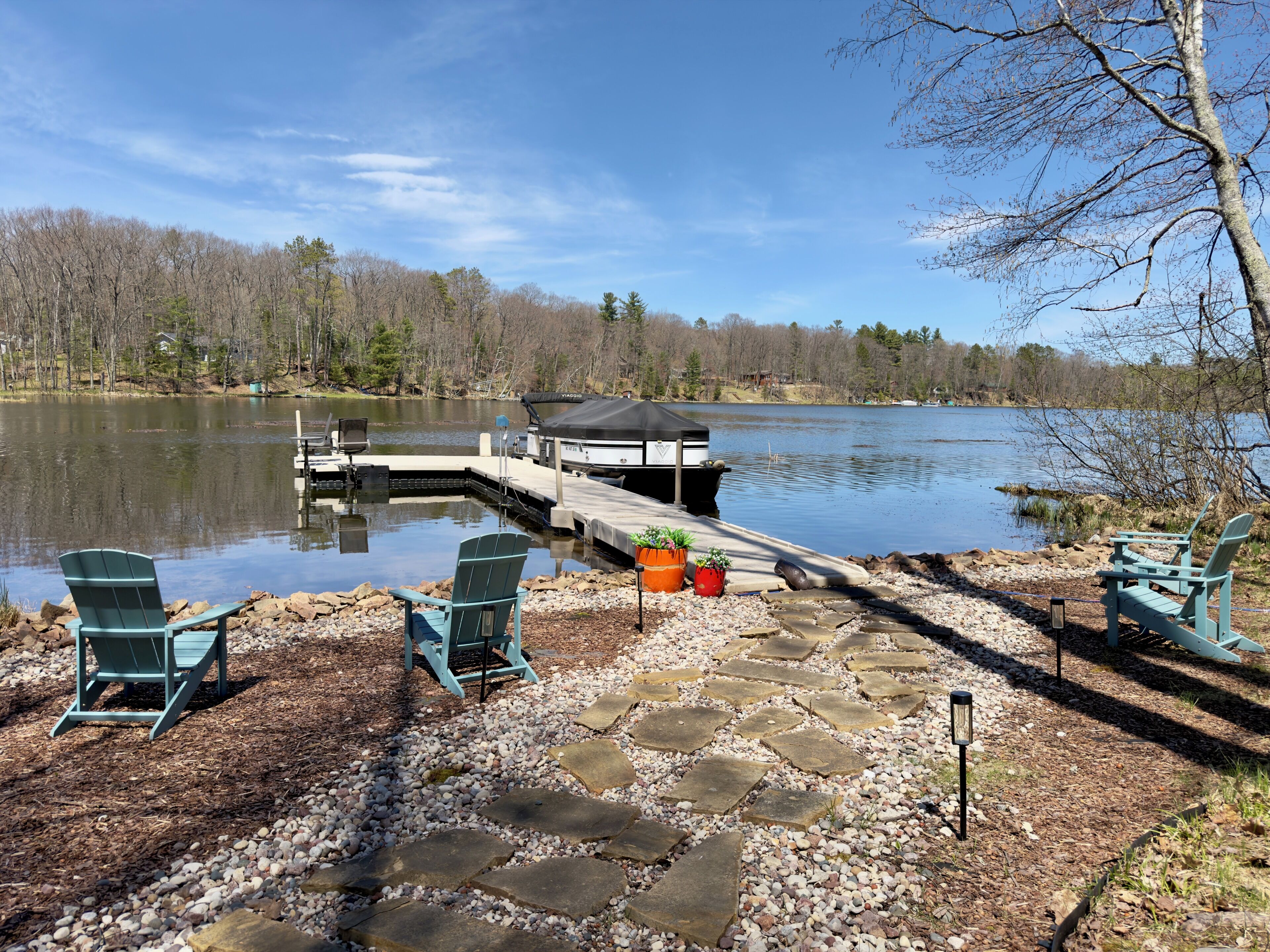 En ankomstbro med et overdækket bådende, en sti af sten og to Adirondack-stole.