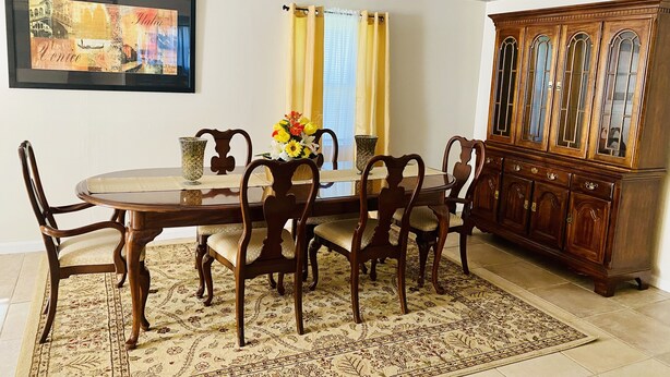 A dining area with a wooden table, chairs, a floral centerpiece, and a cabinet with glass doors. - Cozy relaxation home in the heart of Cocoa (Cocoa)