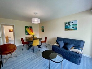 A living room with a blue sofa, a dining table with chairs, and artwork on the walls.