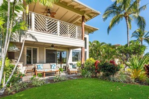 A two-story house with a covered porch, outdoor seating area, and lush tropical landscaping.