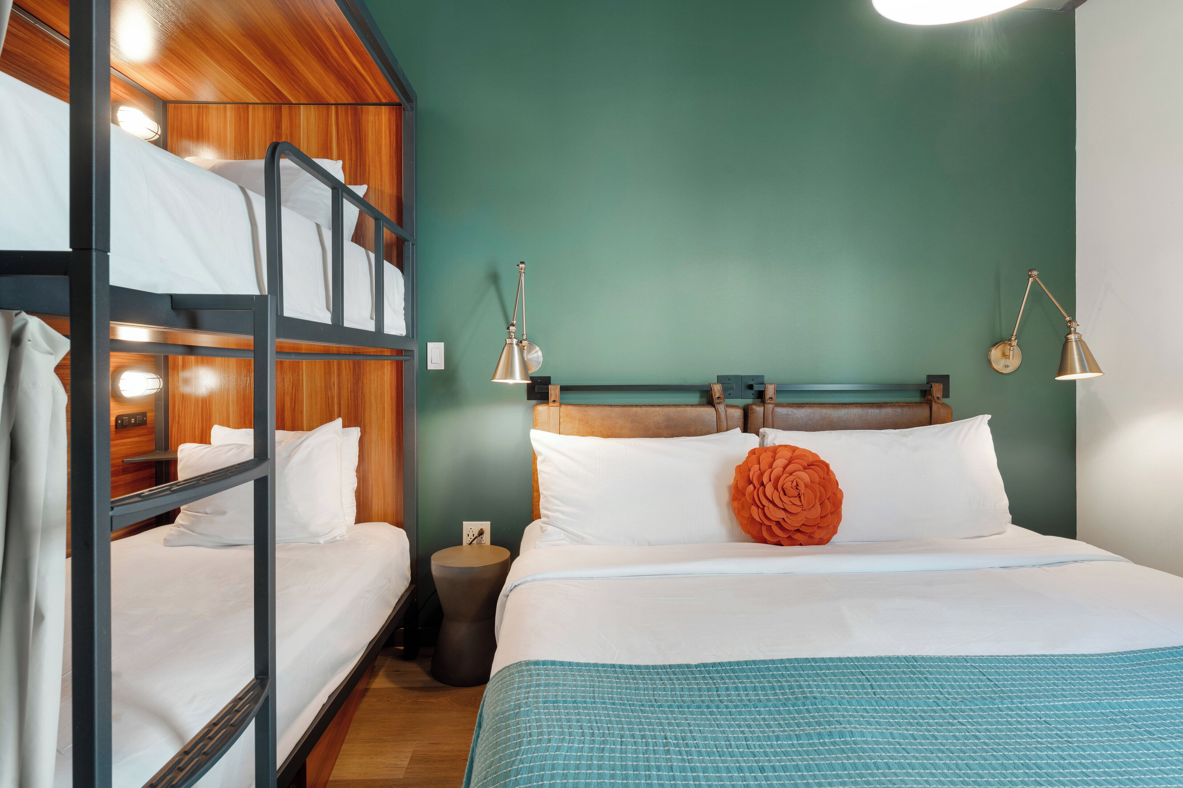 A bunk bed room with a wooden headboard, a single bed with white bedding and an orange pillow, and two bedside lamps.