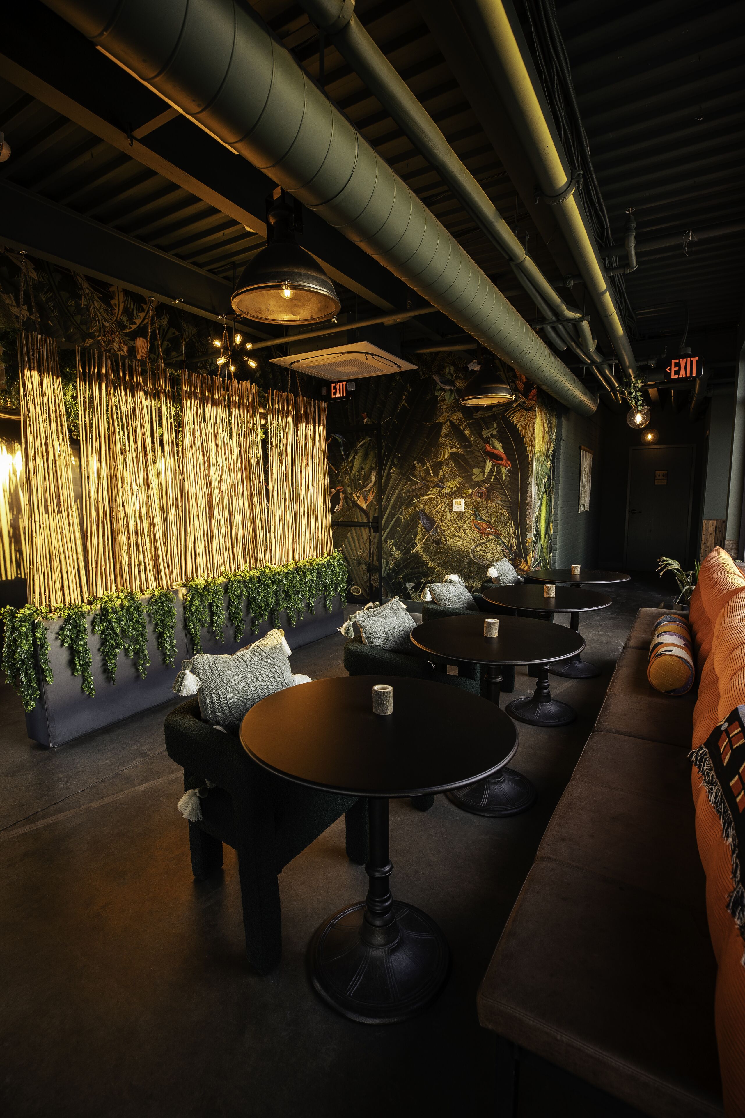 A dimly lit lounge area with round tables, cushioned seating, and a decorative wall with vertical elements.