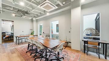 A spacious conference room with a large wooden table, white chairs, and a patterned rug.