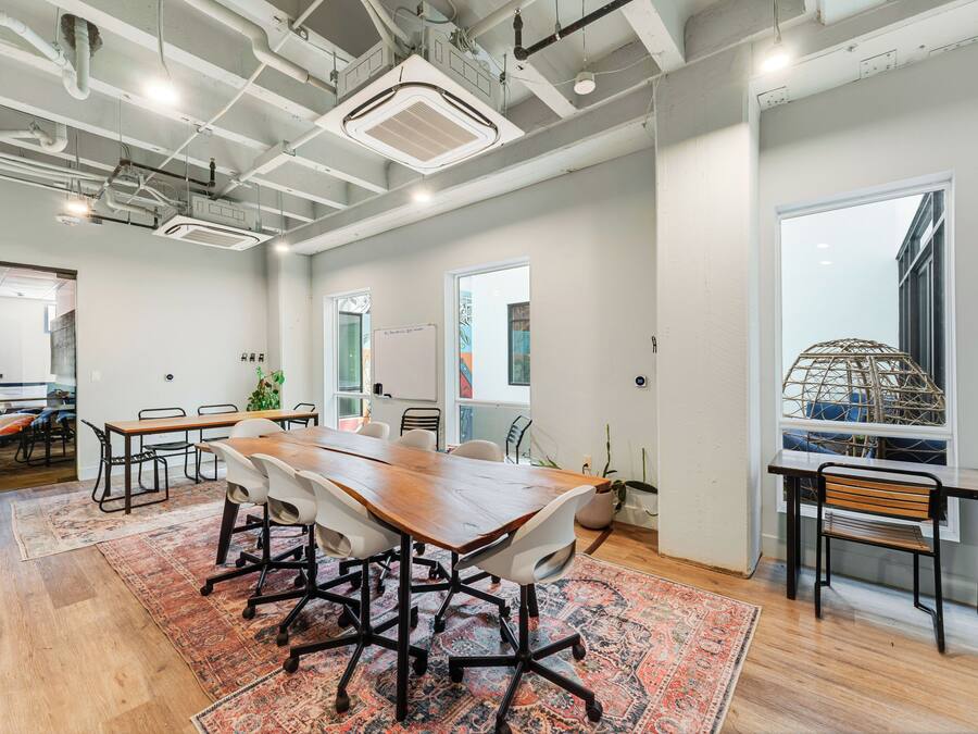 A spacious conference room with a large wooden table, white chairs, and a patterned rug.