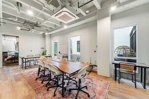 A spacious conference room with a large wooden table, white chairs, and a patterned rug.