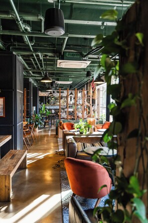 A modern interior with exposed pipes, wooden furniture, and hanging plants.