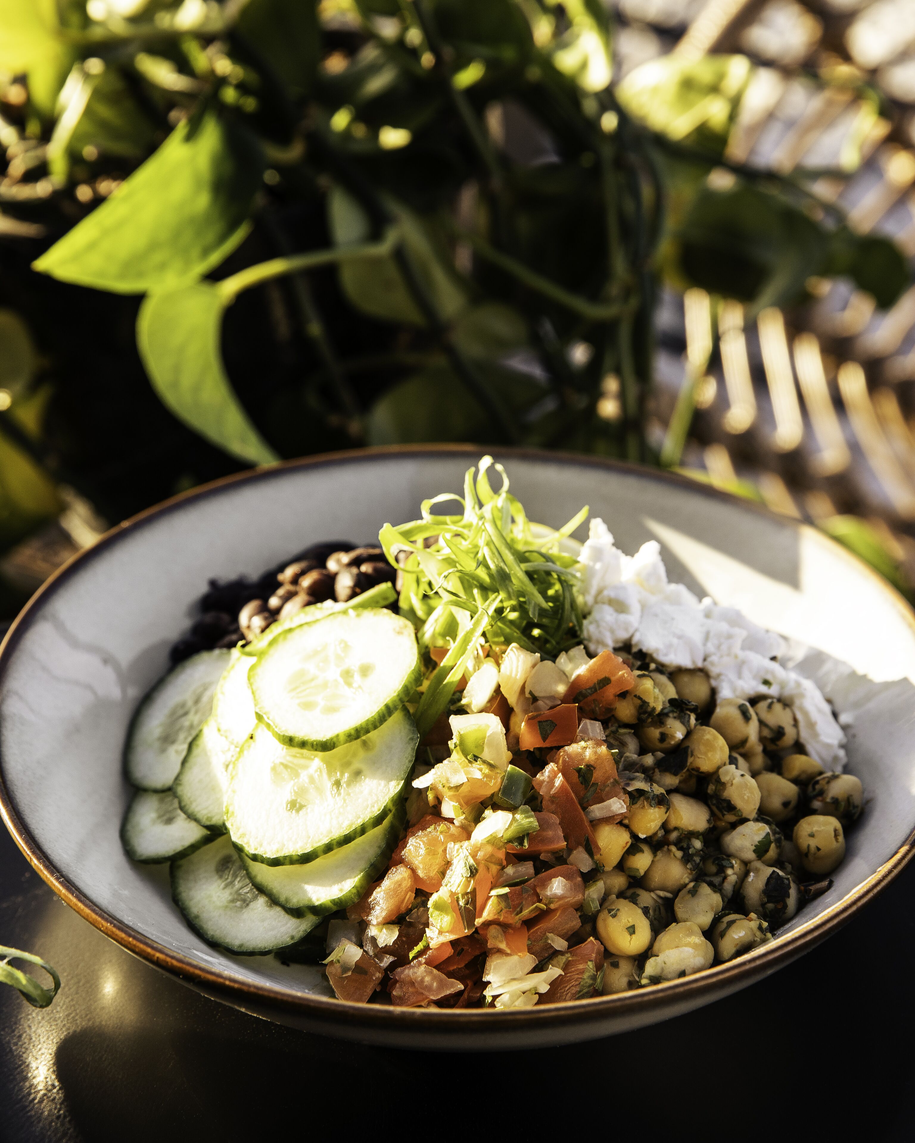 Une salade composée de concombres, de pois chiches et d’autres légumes, servie dans un bol posé sur une assiette.