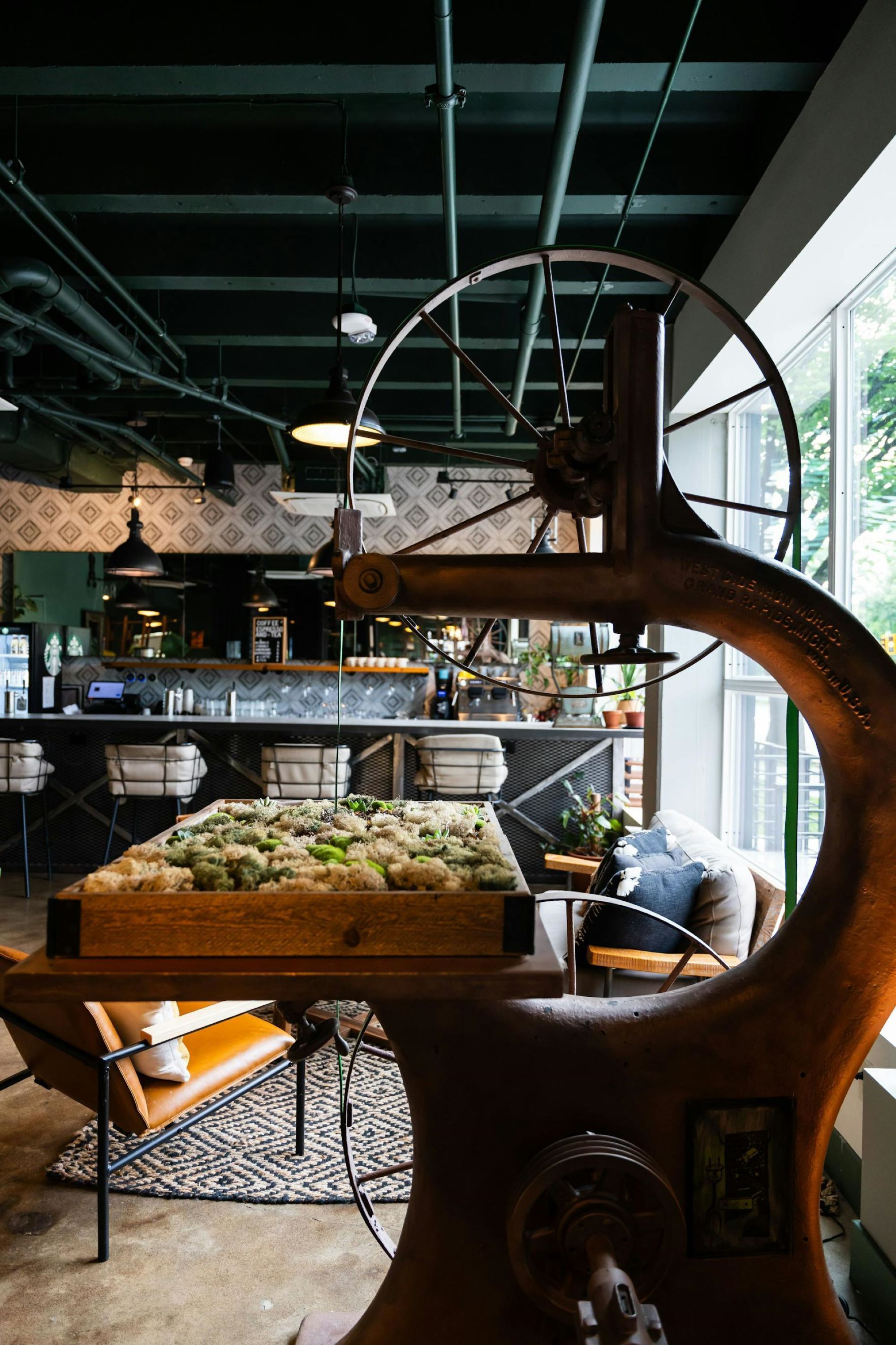 A vintage mechanical press in a modern cafe setting with a bar area, seating, and large windows.