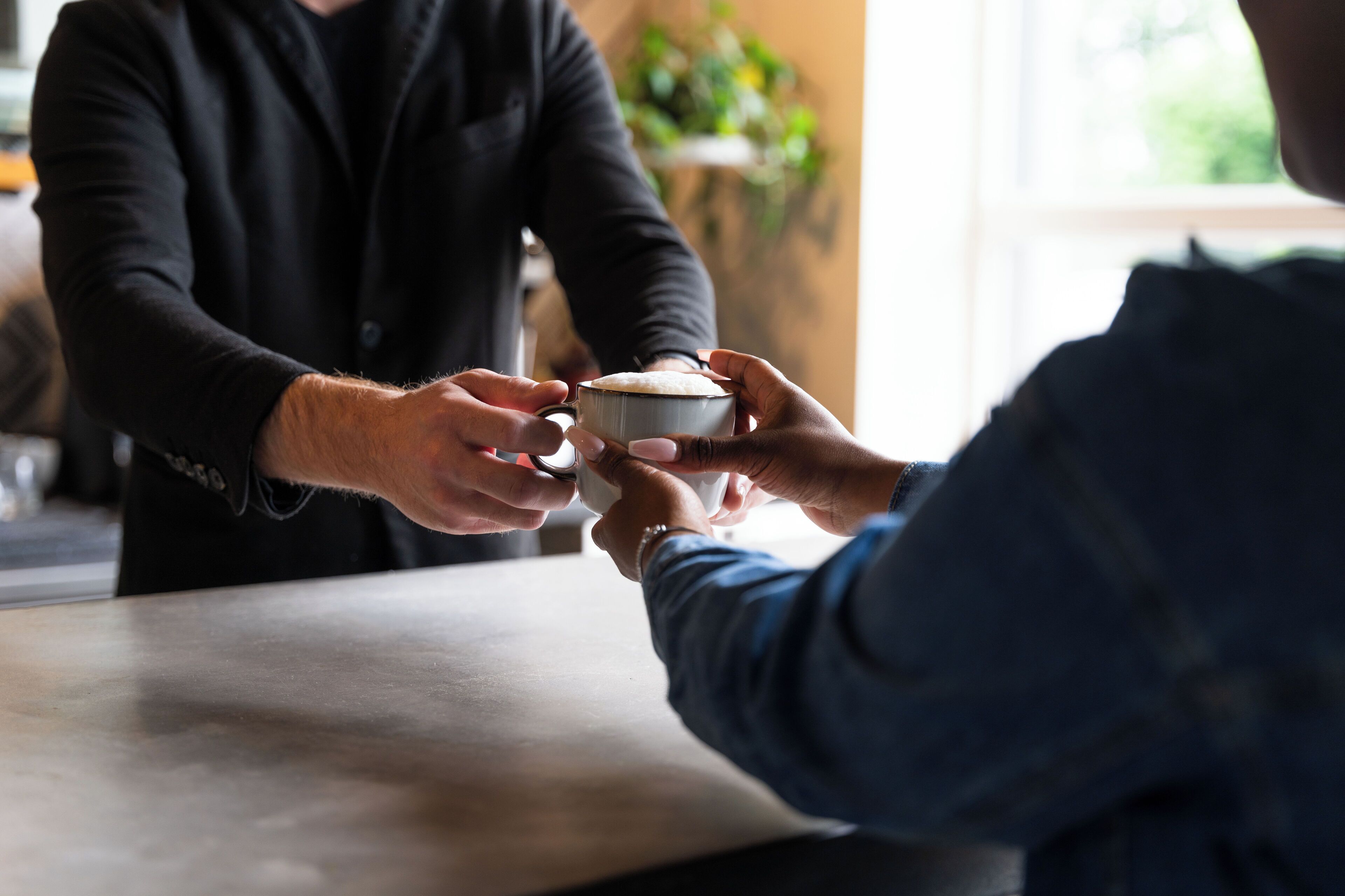 A person handing over a cup to another person at a counter.