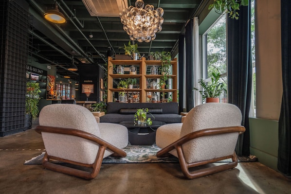 A cozy living area with a sofa, two rocking chairs, a coffee table, and a bookshelf filled with plants and books.