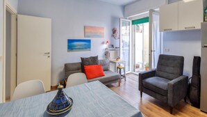 Ein Wohnzimmer mit einer Couch, einem Esstisch und einem Stuhl. Ein Fenster bietet Blick ins Freie.